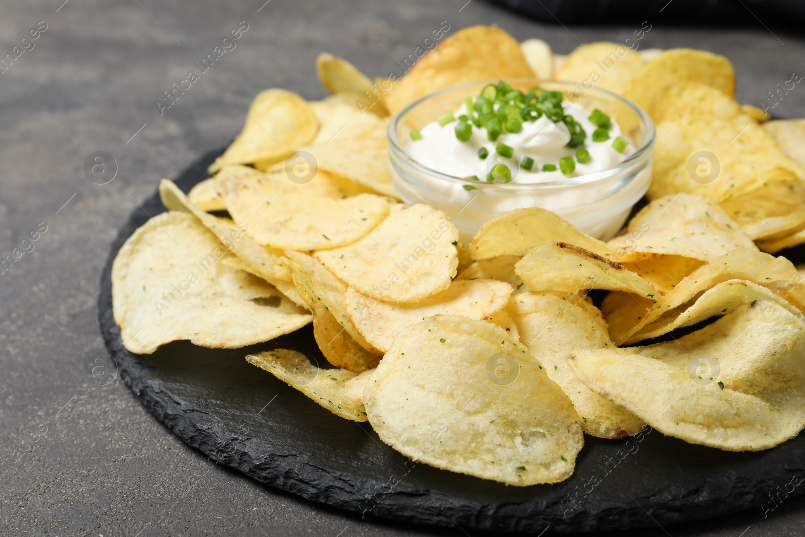 Photo of Sour cream in dipping saucer and chips on grey stone background