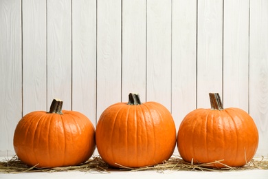 Photo of Ripe orange pumpkins and straw on table against white wooden background. Space for text