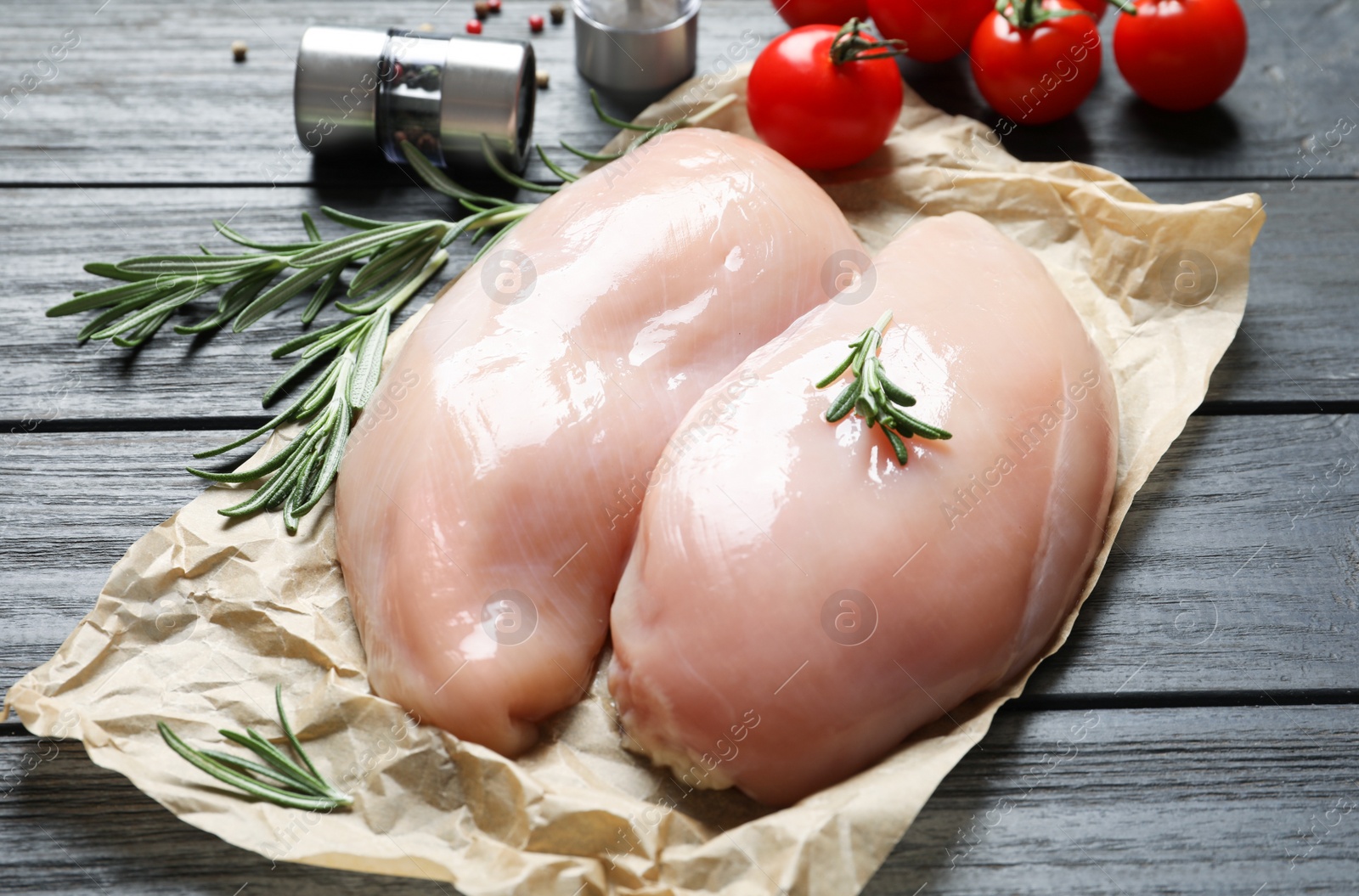 Photo of Parchment with raw chicken breasts and rosemary on wooden table