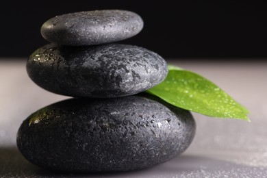 Photo of Wet spa stones and green leaf on grey background, closeup