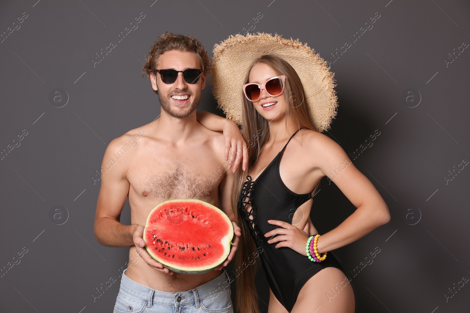 Photo of Young couple in beachwear with watermelon on dark background