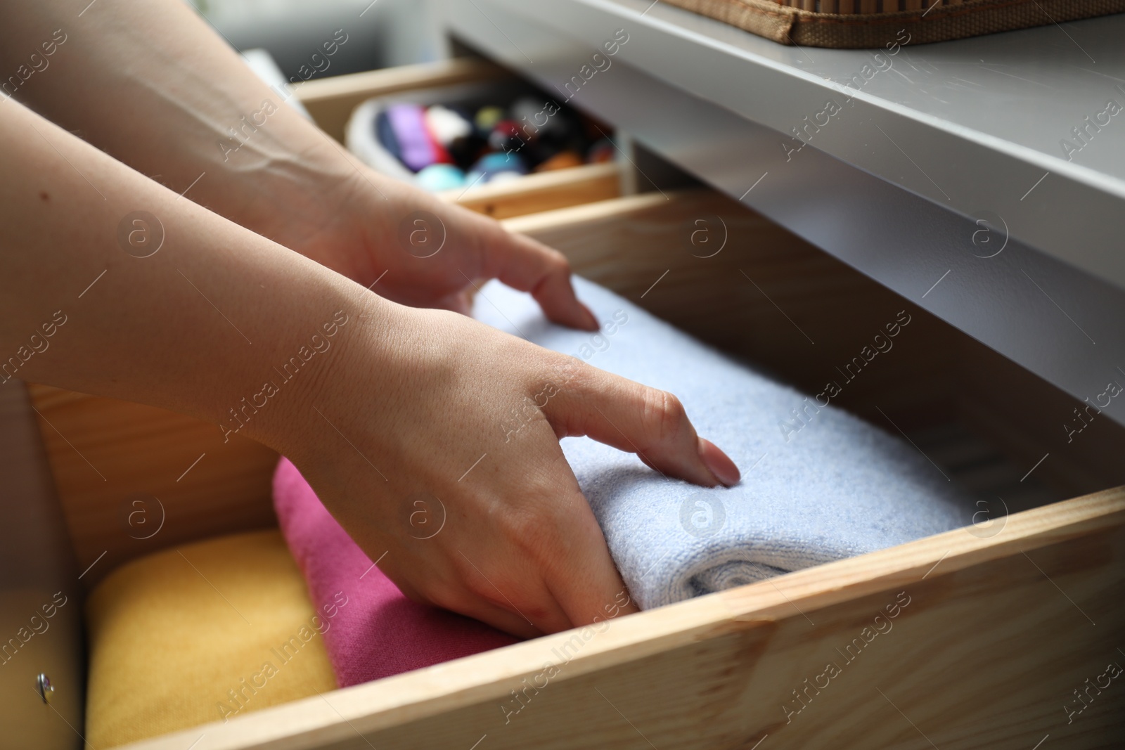 Photo of Woman putting folded clothes into drawer indoors, closeup