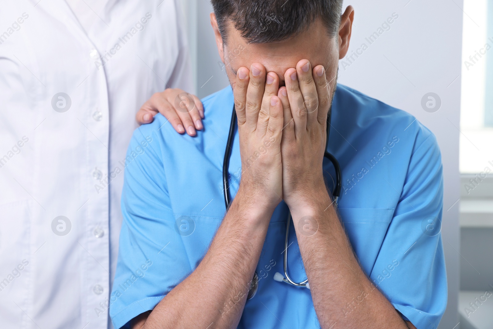 Photo of Doctor covering his face with hands while colleague comforting him in hospital