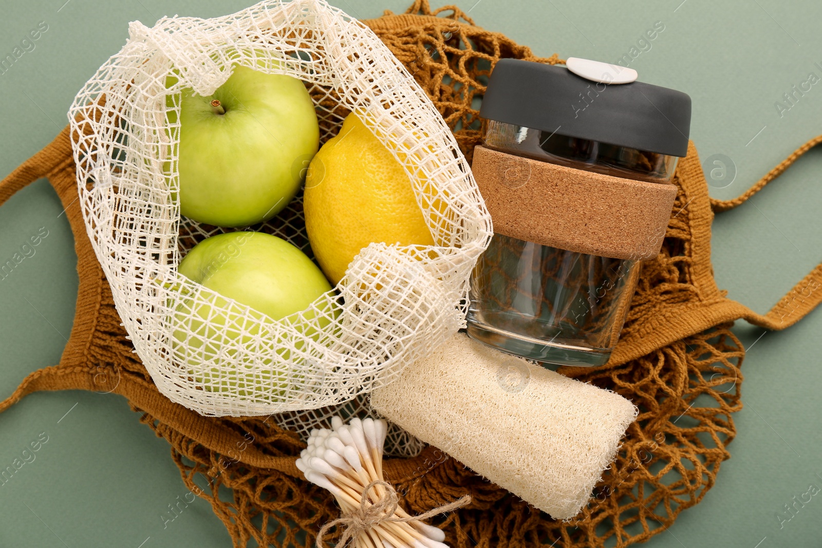 Photo of Fishnet bag with different items on pale green background, top view. Conscious consumption