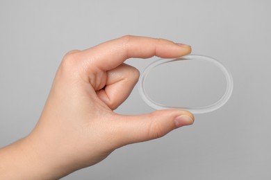 Woman holding diaphragm vaginal contraceptive ring on grey background, closeup