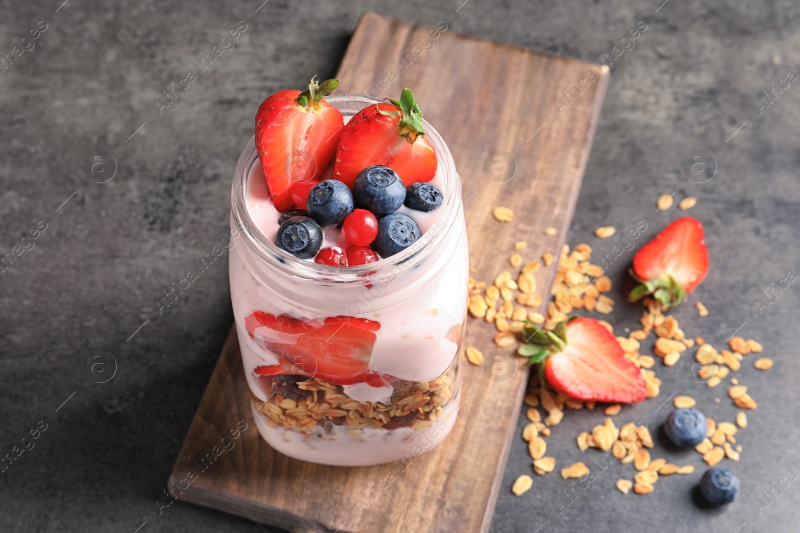 Photo of Mason jar with yogurt, berries and granola on table