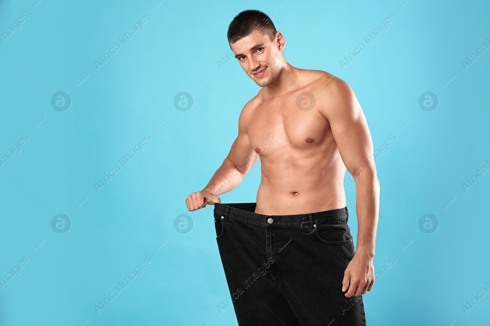 Photo of Young man with slim body in old big size jeans on light blue background, space for text