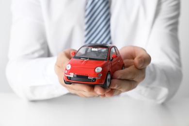 Photo of Male insurance agent holding toy car, closeup