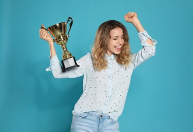 Photo of Portrait of happy young woman with gold trophy cup on blue background