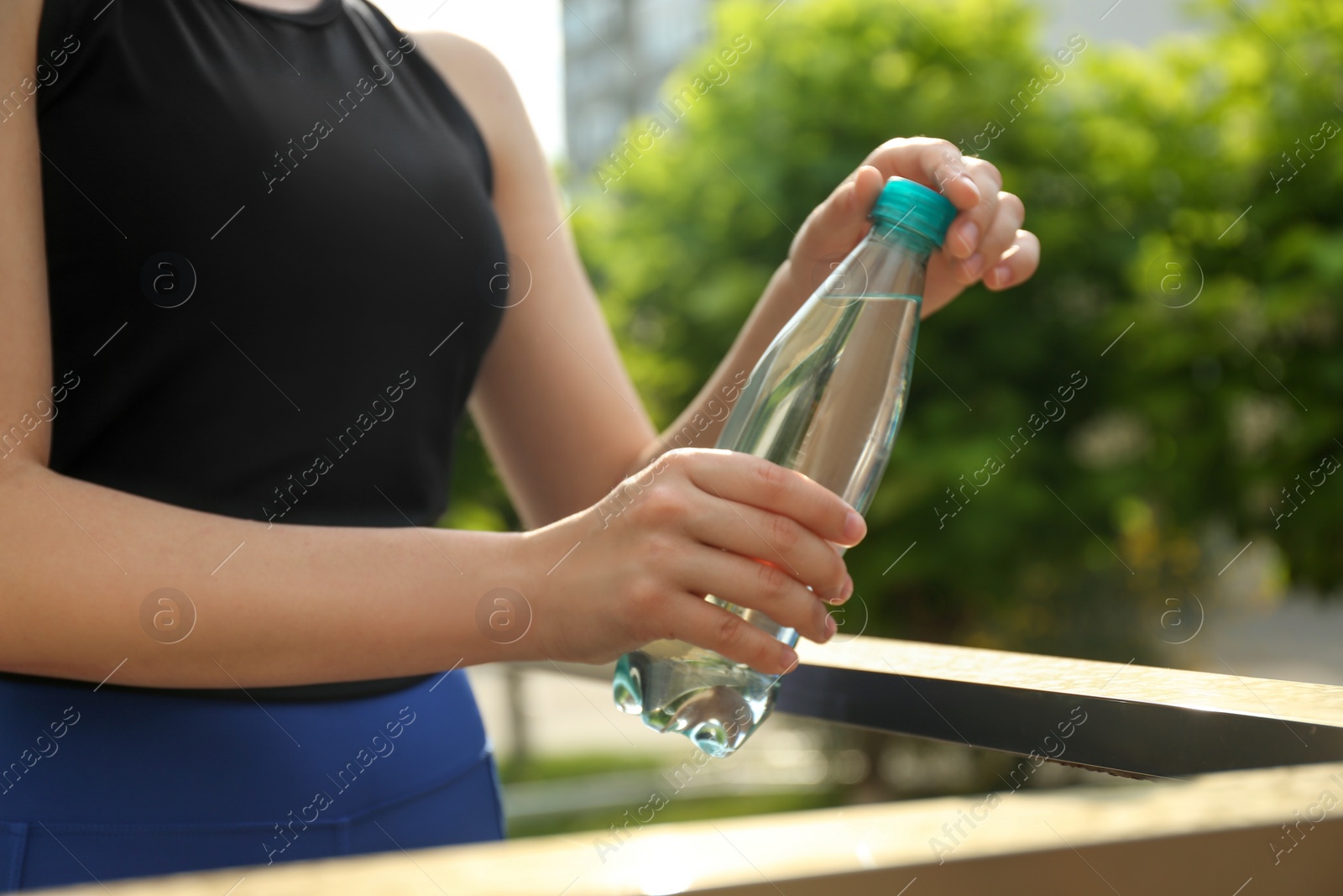 Photo of Young woman with bottle of pure water outdoors, closeup