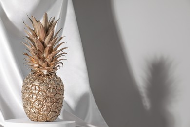Photo of Golden pineapple and white silk fabric on light grey background. Space for text