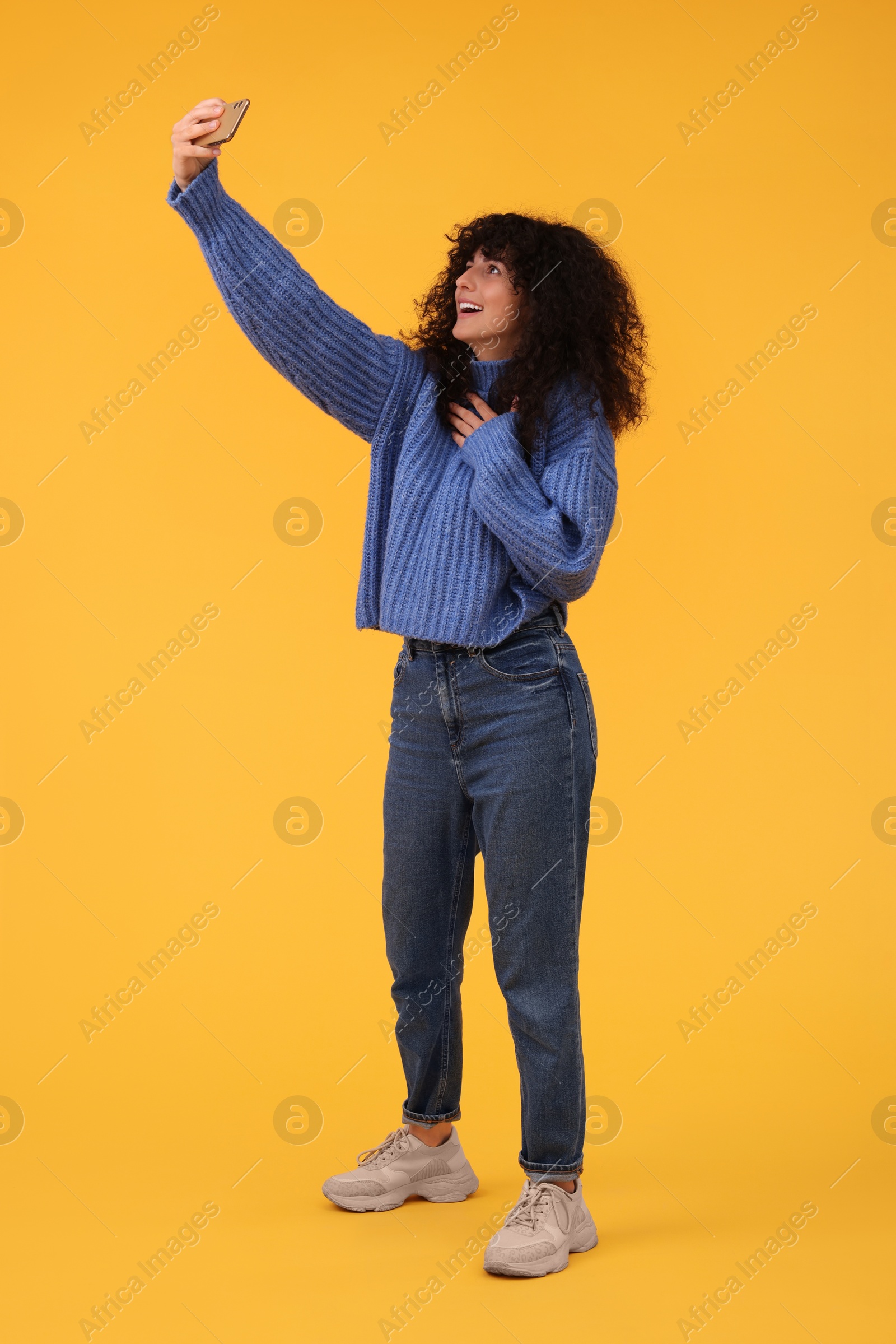 Photo of Beautiful young woman taking selfie with smartphone on orange background