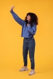 Beautiful young woman taking selfie with smartphone on orange background