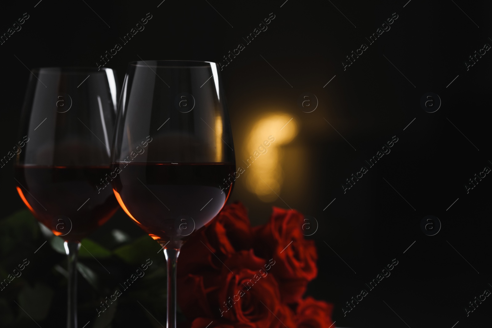 Photo of Glasses of red wine and rose flowers on blurred background, space for text. Romantic atmosphere