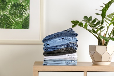 Photo of Stack of different jeans on table against light wall in living room