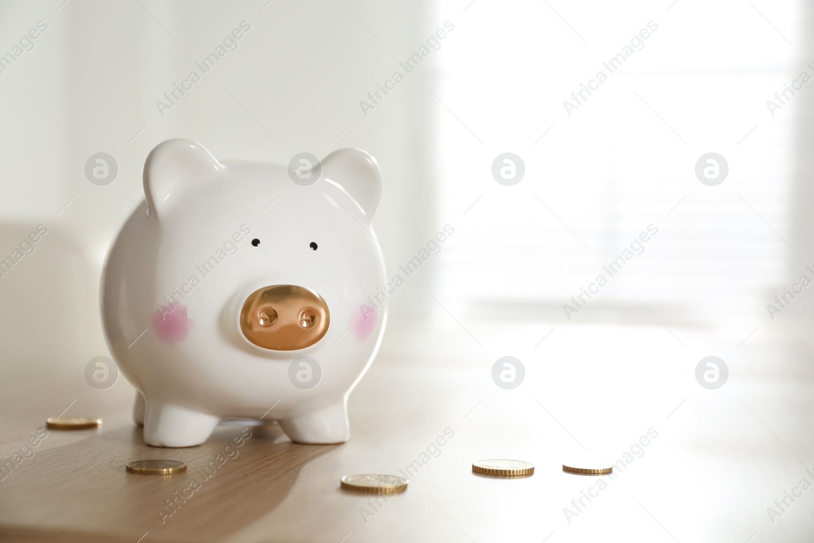 Photo of Piggy bank and coins on wooden table indoors. Space for text