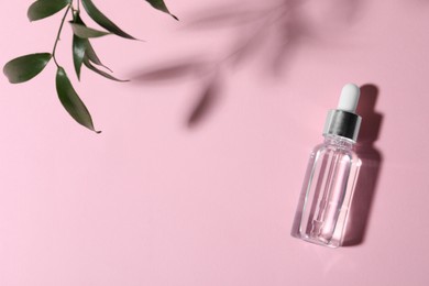 Photo of Bottle of cosmetic oil and green leaves on pink background, top view. Space for text