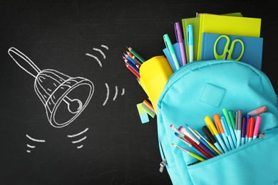 Backpack full of stationery and drawn school bell on blackboard surface, flat lay