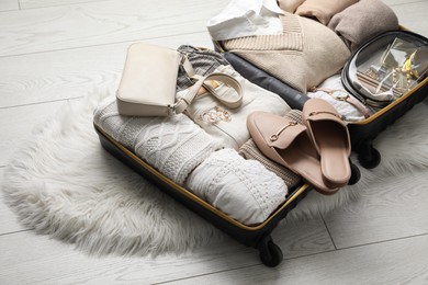 Photo of Open suitcase with folded clothes, shoes and accessories on floor