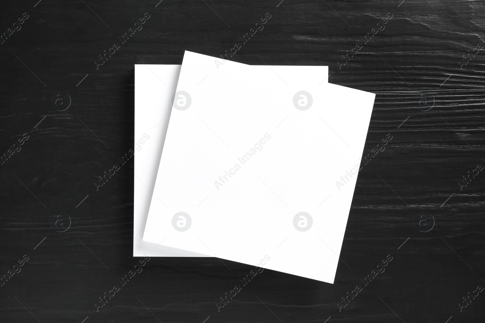 Photo of Stack of blank paper sheets for brochure on black wooden background, top view. Mock up