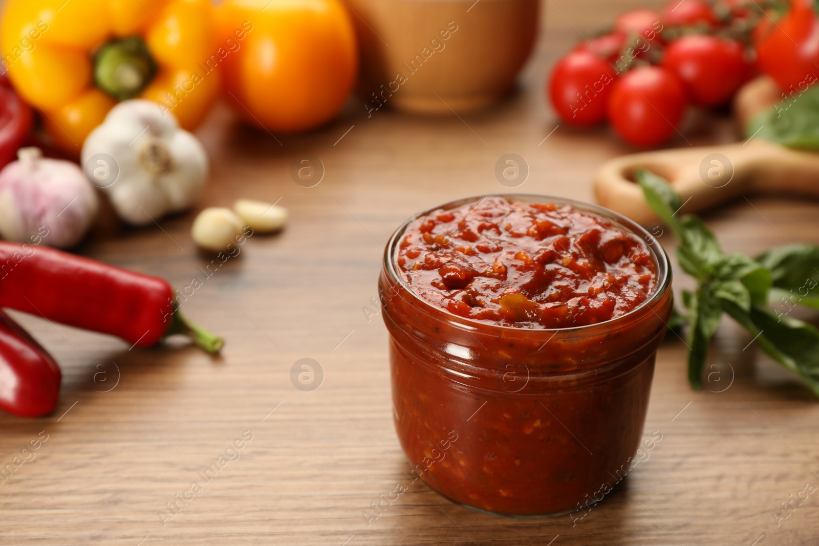 Photo of Glass jar of tasty adjika and ingredients on wooden table, space for text