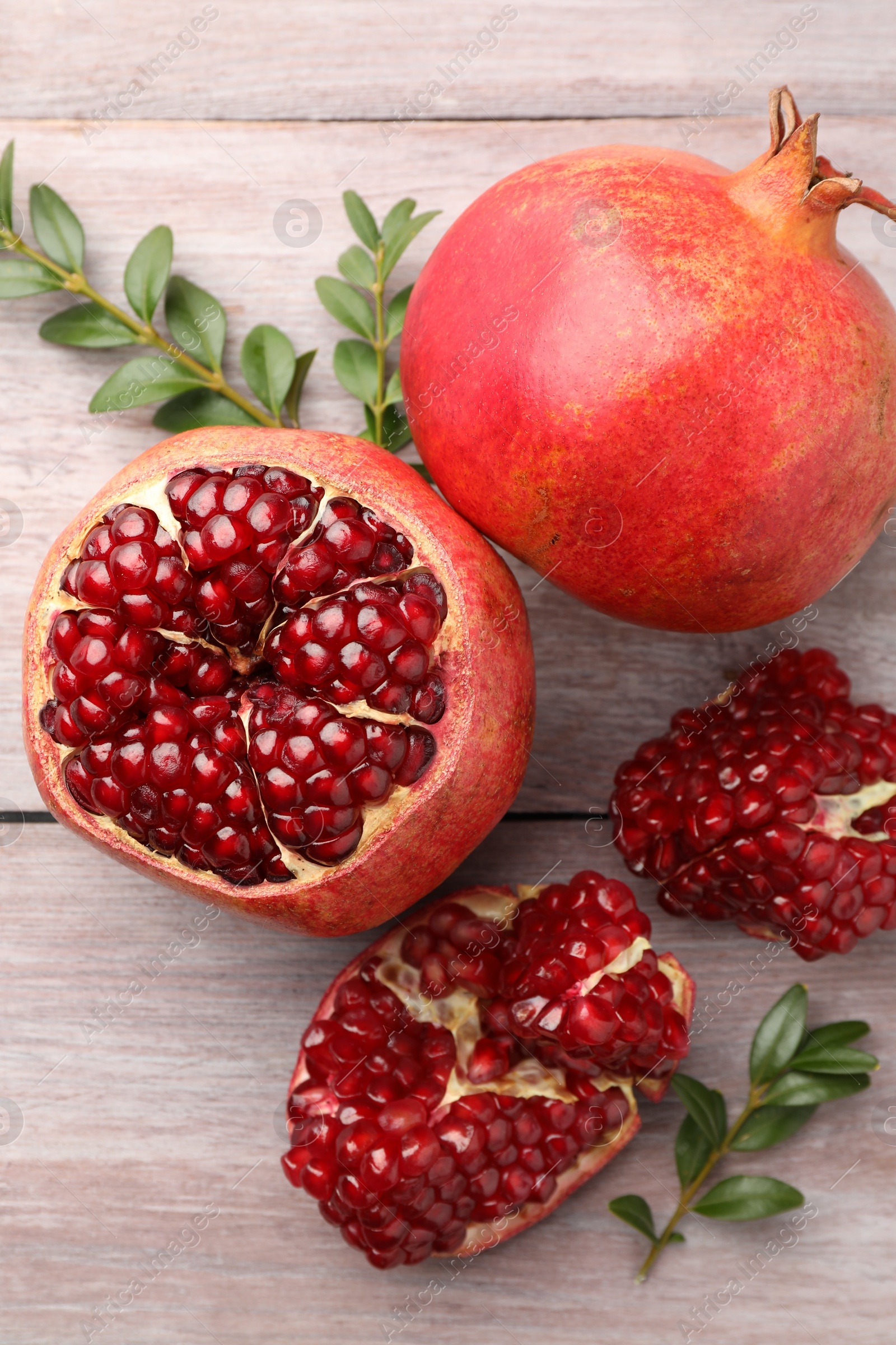 Photo of Fresh pomegranates and green leaves on wooden table, flat lay