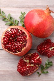 Photo of Fresh pomegranates and green leaves on wooden table, flat lay