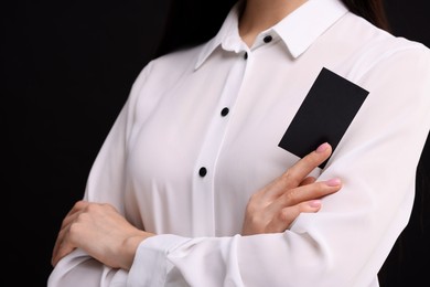 Woman holding blank business card on black background, closeup. Space for text