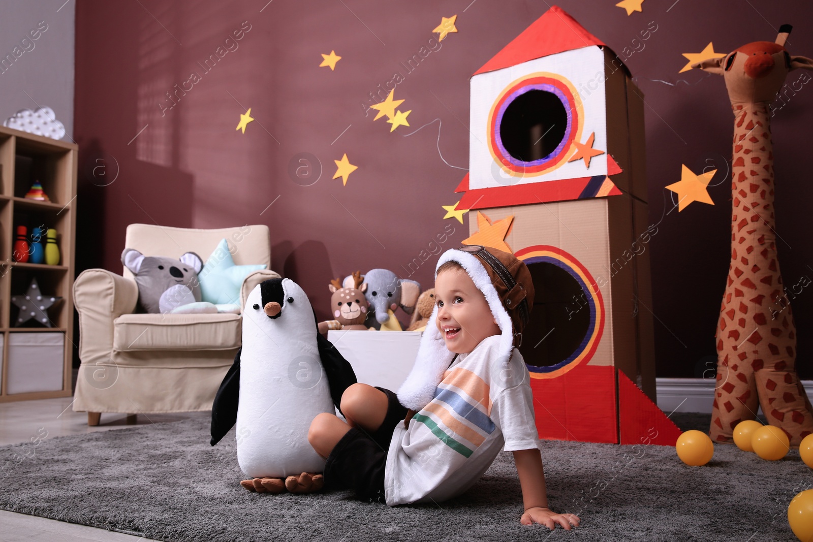 Photo of Cute little boy playing on floor near cardboard rocket  at home. Child's room interior