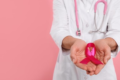 Photo of Doctor with stethoscope holding pink ribbon on color background, closeup and space for text. Breast cancer awareness