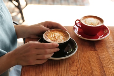 Woman with cup of fresh aromatic coffee at table, closeup