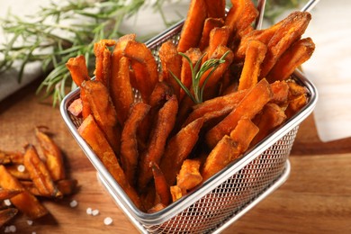 Photo of Frying basket with sweet potato fries and rosemary on wooden table, closeup