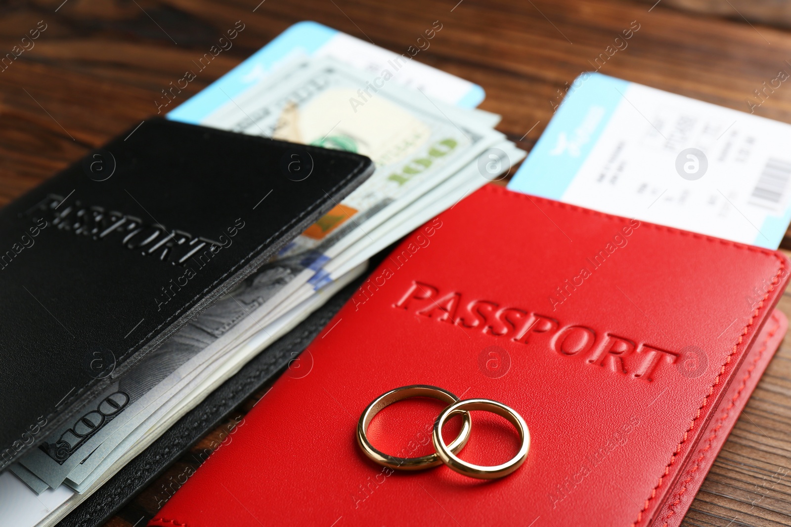 Photo of Honeymoon concept. Two golden rings, passports, money and tickets on wooden table, closeup