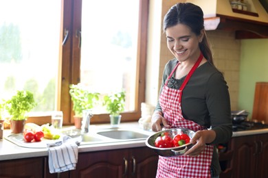 Photo of Young woman holding colander with fresh bell peppers in kitchen, space for text