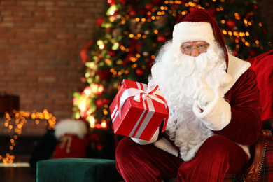 Photo of Santa Claus with gift near Christmas tree indoors