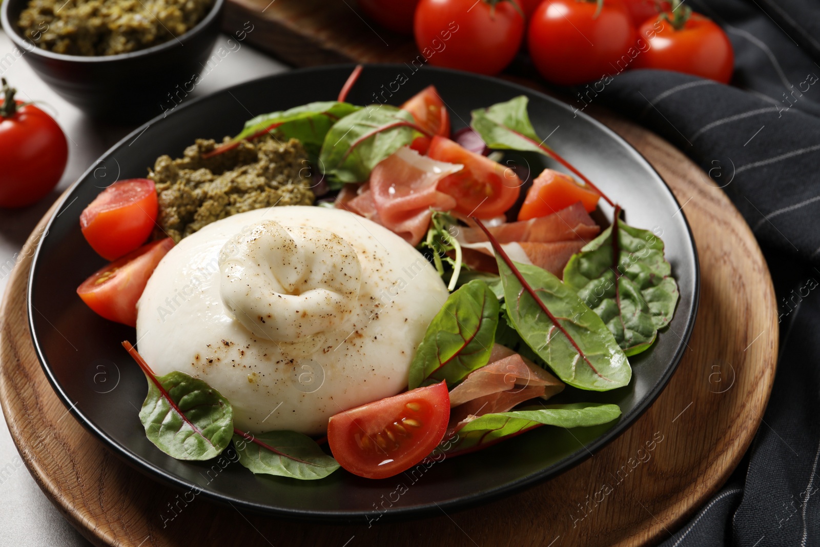 Photo of Delicious burrata salad with tomatoes and prosciutto served on table, closeup