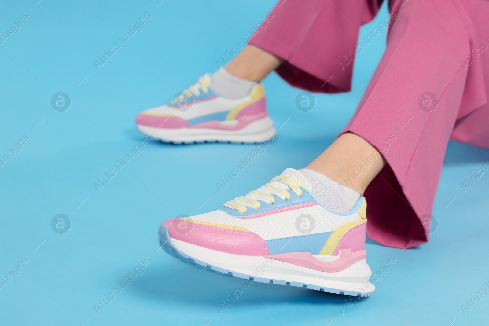 Photo of Woman wearing pair of new stylish sneakers on light blue background, closeup