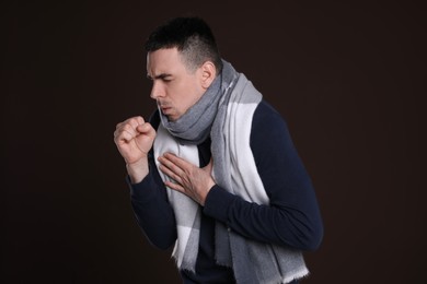 Photo of Young man with scarf coughing on dark background. Cold symptoms