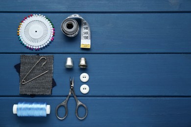 Photo of Flat lay composition with thimbles and different sewing tools on blue wooden table. Space for text