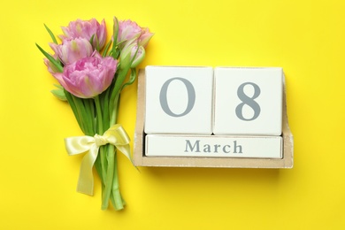 Photo of Wooden block calendar with date 8th of March and tulips on yellow background, flat lay. International Women's Day