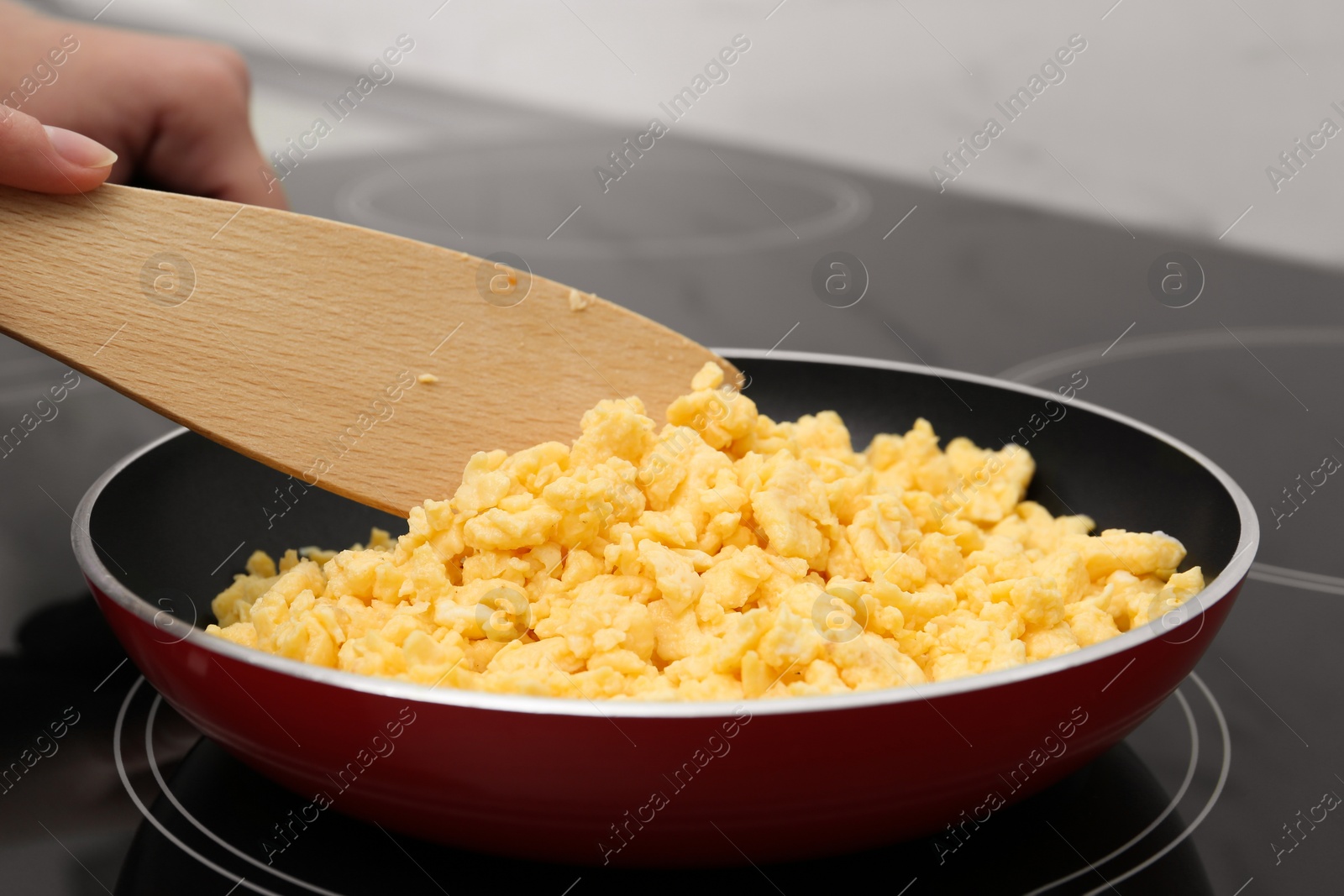 Photo of Woman cooking tasty scrambled eggs in frying pan on stove, closeup