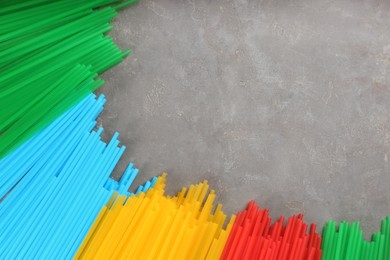 Colorful plastic drinking straws on grey stone table, flat lay. Space for text