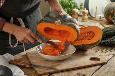 Woman removing seeds from raw pumpkin at wooden table in kitchen, closeup