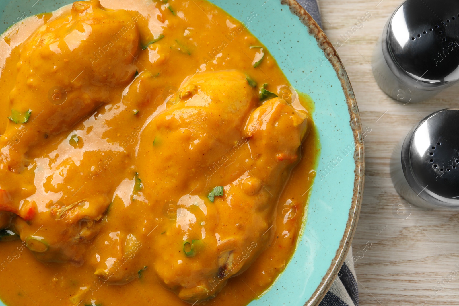 Photo of Tasty chicken curry, salt and pepper shakers on wooden table, flat lay