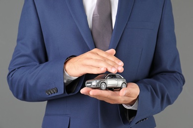 Insurance agent holding toy car on gray background, closeup