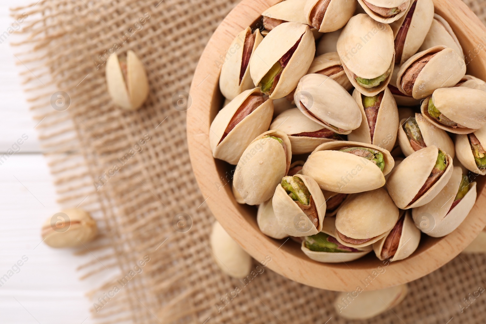Photo of Tasty pistachios in bowl on white wooden table, top view. Space for text
