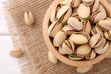 Tasty pistachios in bowl on white wooden table, top view. Space for text