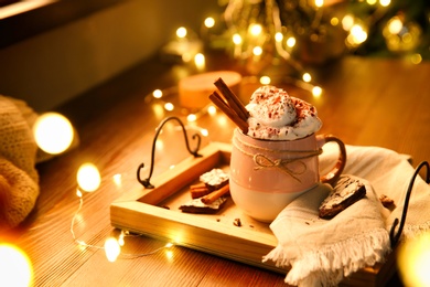 Photo of Tasty hot drink with whipped cream and Christmas lights on wooden table