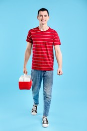 Man with cool box walking on light blue background