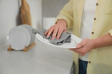 Woman wiping plate with towel at white marble table in kitchen, closeup